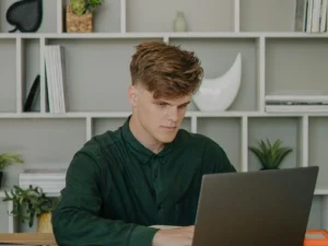 Boy staring at a laptop with a shelf background